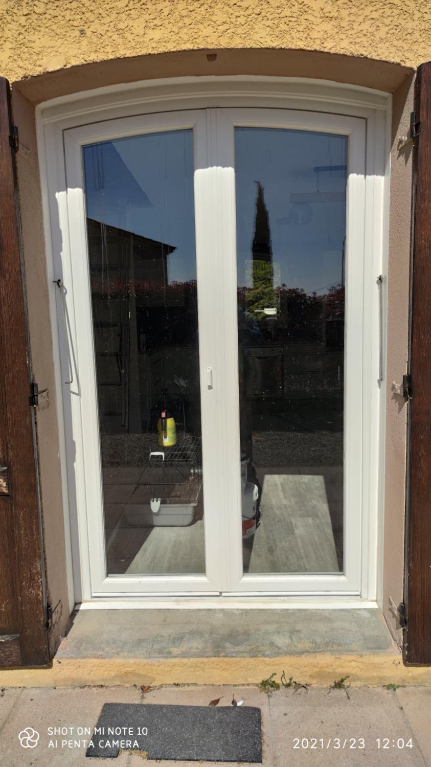 Porte-fenêtre cintrée blanche entre deux volets bois